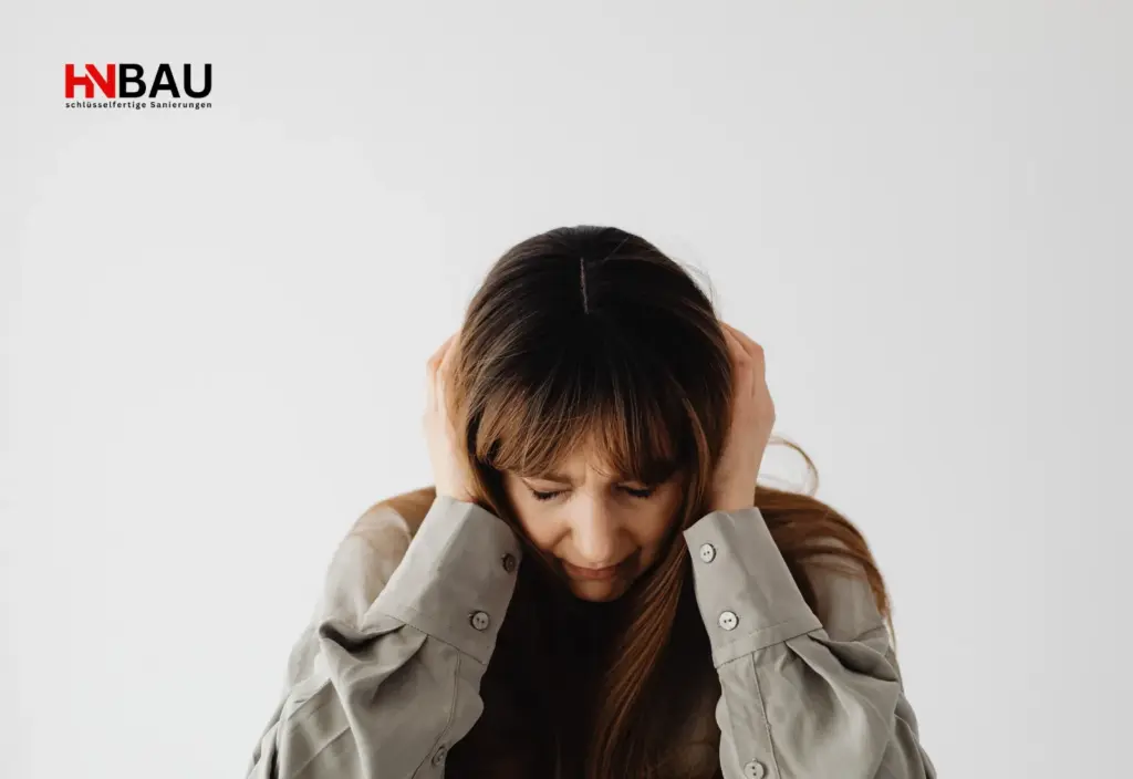 Frau hält sich frustriert den Kopf, symbolisiert Stress und typische Fehler bei Haussanierungen – HN-Bau Sanierungen Niederrhein.