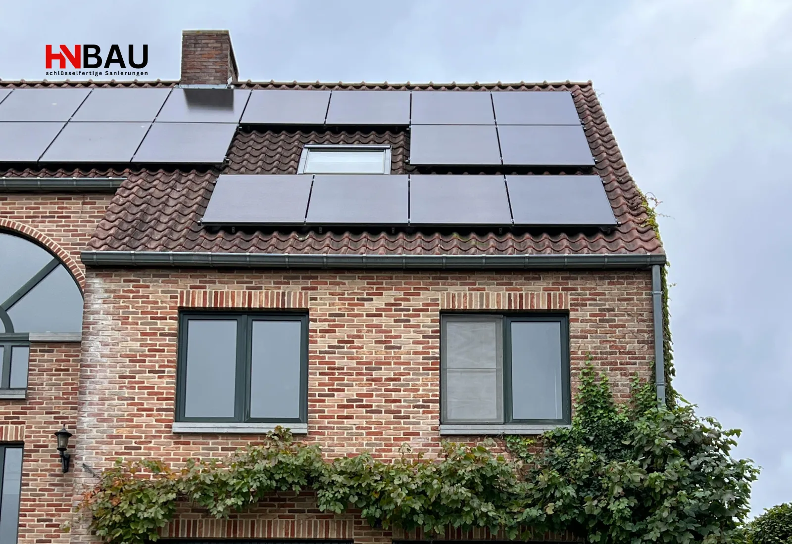 Ein Einfamilienhaus mit roter Klinkerfassade und anthrazitfarbenen Fenstern, auf dessen Schrägdach mehrere schwarze Photovoltaik-Module montiert sind. Die moderne PV-Anlage erstreckt sich über große Teile der Dachfläche und zeigt eine energieeffiziente, zeitgemäße Nutzung des Gebäudes.