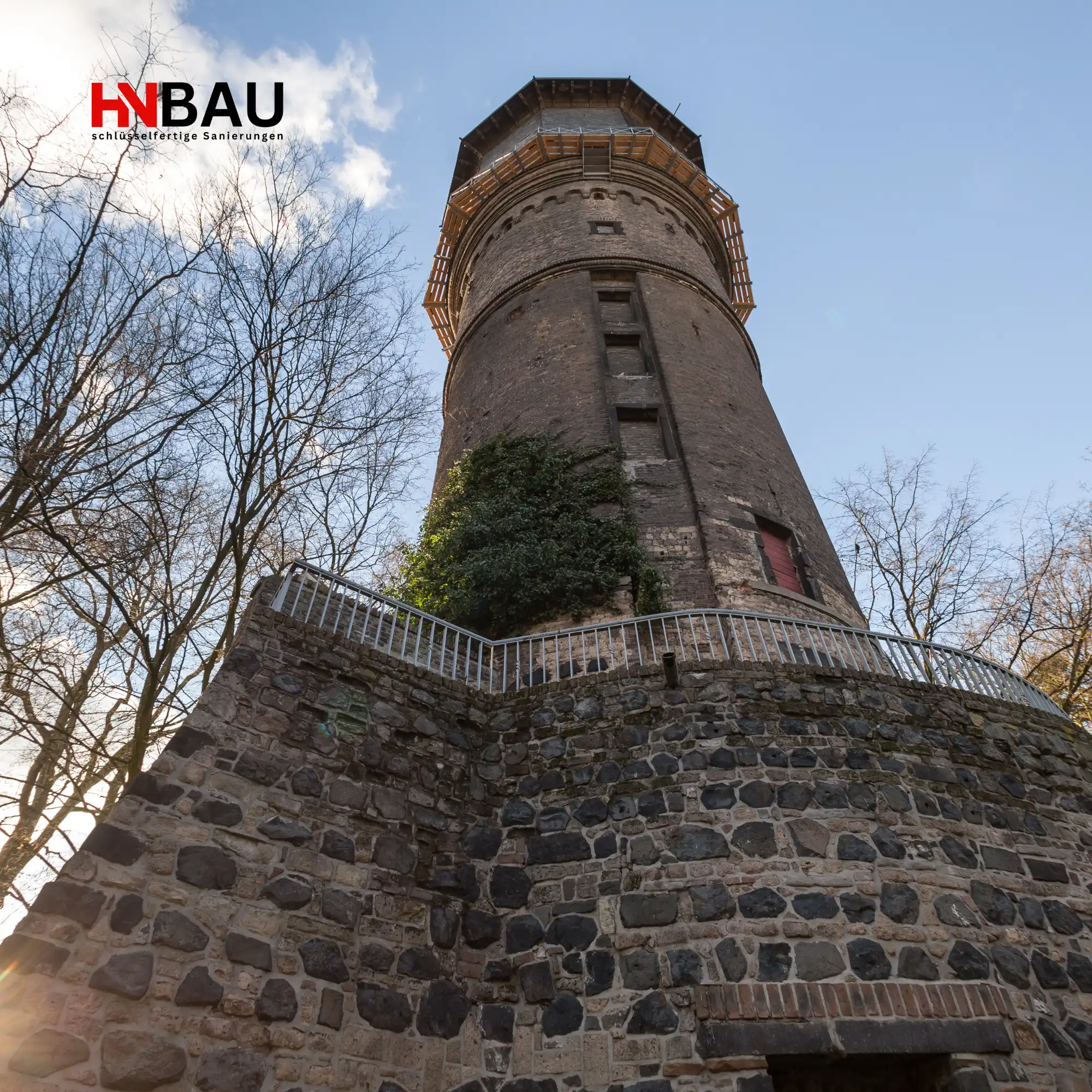 Alter Wasserturm in Neuss, historisches Wahrzeichen der Stadt, umgeben von Bäumen und Natur, fotografiert aus der Froschperspektive – Symbol für regionale Sanierungs- und Handwerkskompetenz von HN-Bau.