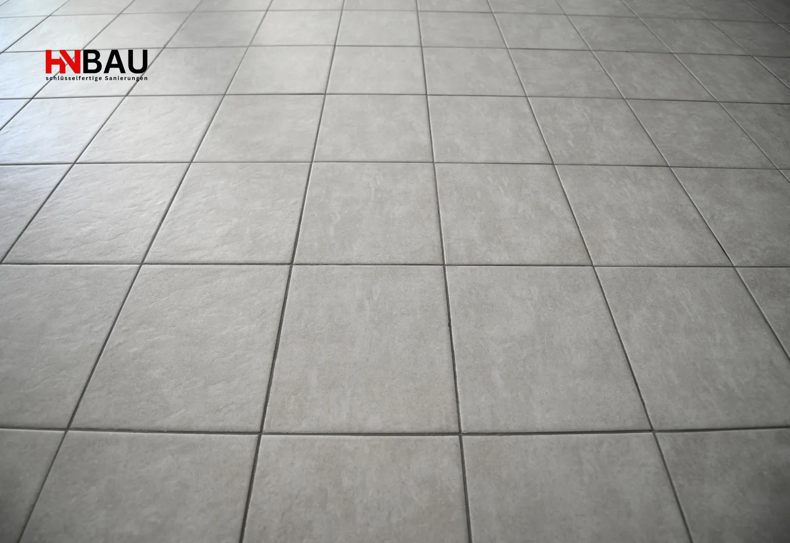 Neu verlegte, graue Bodenfliesen mit sauber ausgeführten Fugenlinien; moderner und langlebiger keramischer Bodenbelag.