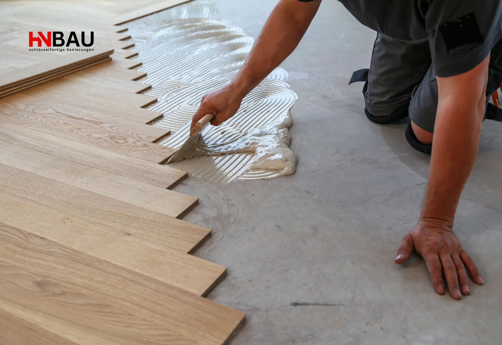 Handwerker verlegt neuen Parkettboden und verteilt Kleber mit einer Zahnkelle auf dem Untergrund; präzise Arbeitsschritte beim Bodenlegen.
