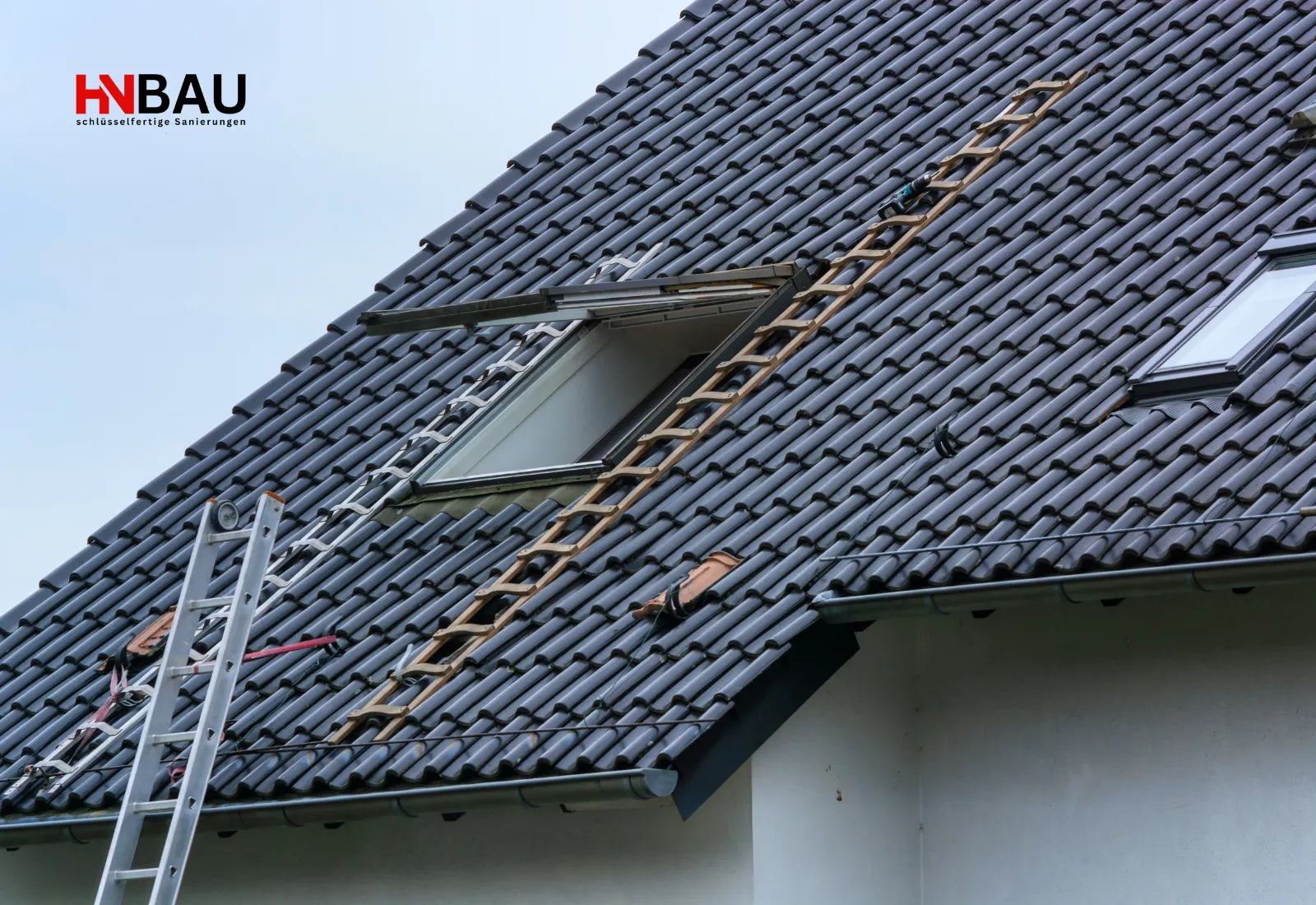 Dachdeckerarbeiten an einem geneigten Ziegeldach mit geöffnetem Dachfenster, Leitern und sichtbaren Sanierungsbereichen. Ein Arbeiter ist nicht im Bild, aber Materialien und Werkzeuge deuten auf eine laufende Dachsanierung hin.