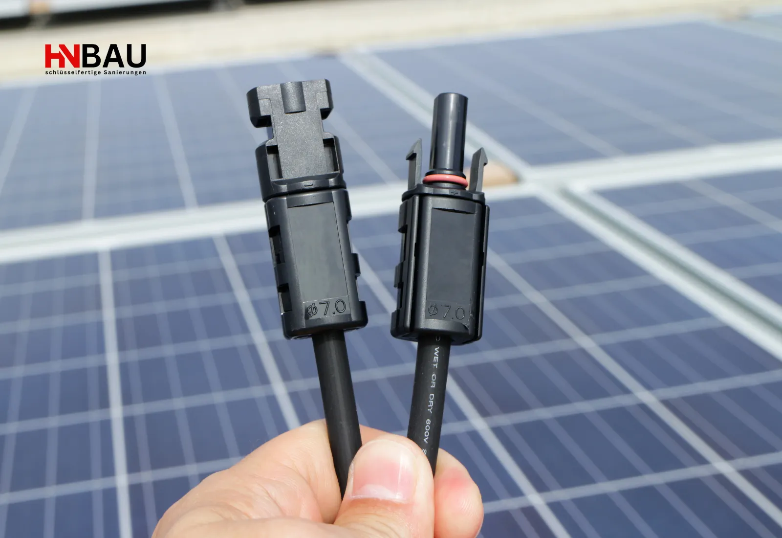 Nahaufnahme von zwei PV-Steckverbindern (MC4) vor einer Photovoltaikanlage auf dem Dach. Die Stecker werden für den sicheren Anschluss von Solarmodulen verwendet und stehen beispielhaft für fachgerechte Elektroarbeiten und PV-Installationen durch HN Bau.