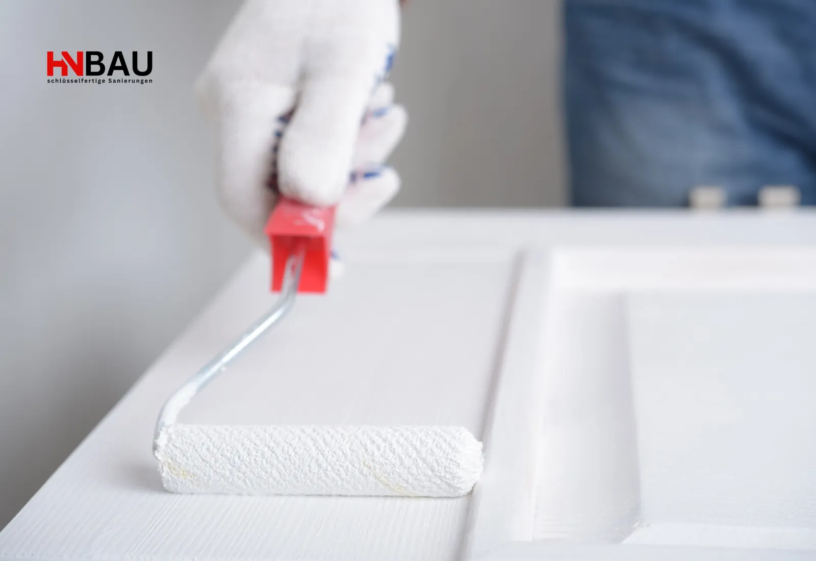 Nahaufnahme einer Lackierarbeit: Handwerker trägt mit einer kleinen Farbrolle weißen Lack auf eine Tür auf.