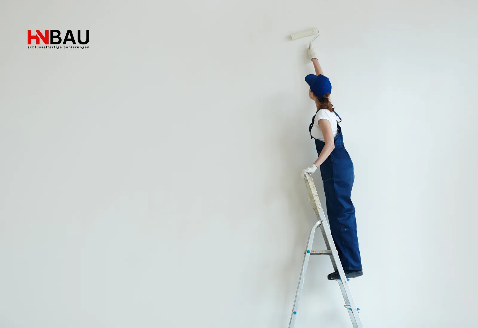 Malerin steht auf einer Leiter und streicht eine Innenwand mit einer Farbrolle, während Renovierungsarbeiten im Raum stattfinden.