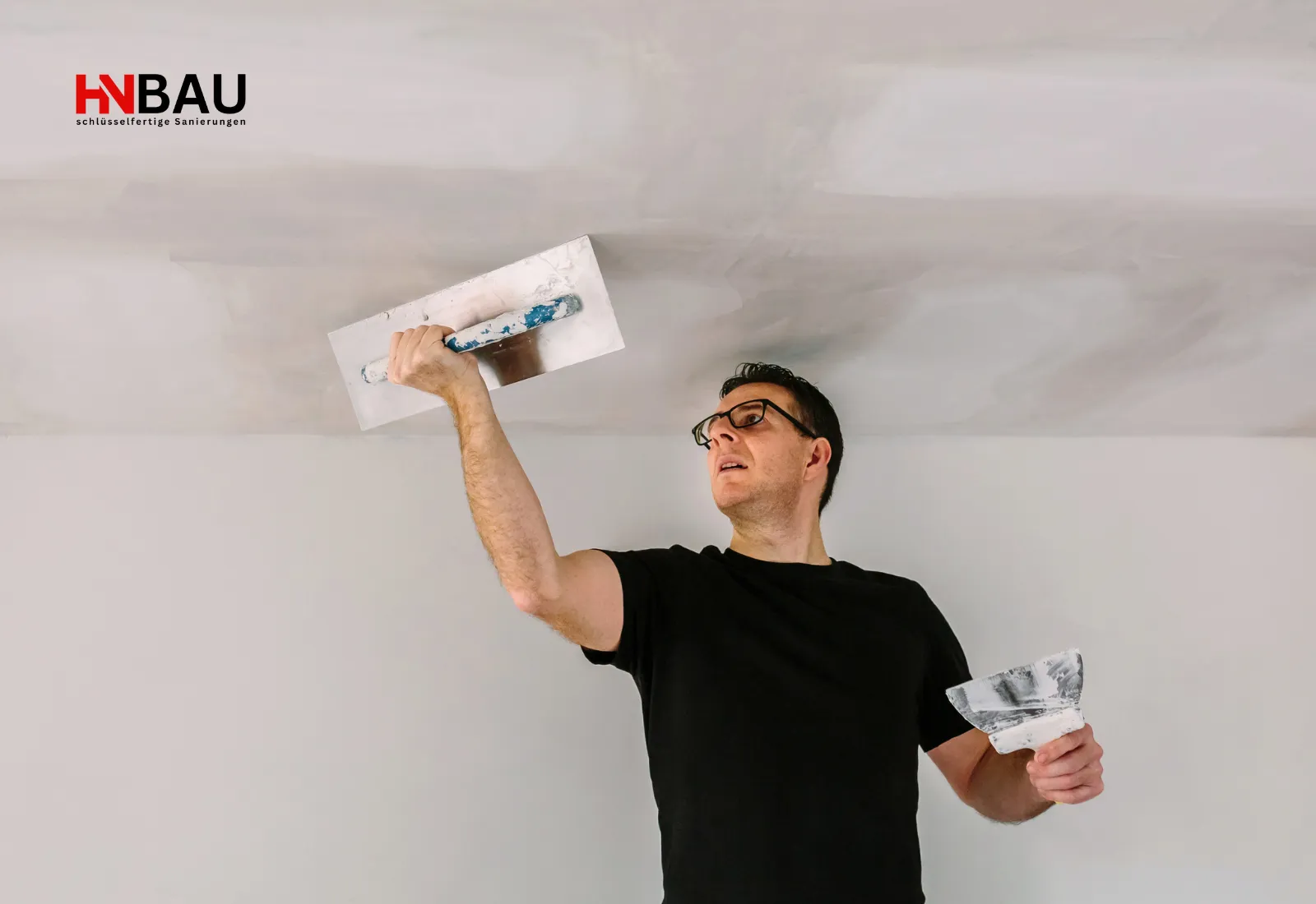 Handwerker spachtelt eine Zimmerdecke mit einer großen Glättkelle und sorgt für eine gleichmäßig glatte Oberfläche bei Renovierungsarbeiten.