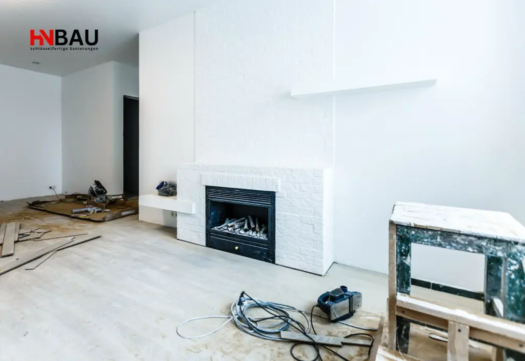 Helles, modernisiertes Wohnzimmer während einer Sanierung mit weiß verkleidetem Kamin, offenliegendem Bodenbelag und Werkzeug auf dem Boden; Renovierungsarbeiten in einem Einfamilienhaus.