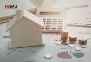 Hausmodell aus Holz auf Finanzunterlagen mit Diagrammen, Taschenrechner und gestapelten Münzen – Symbolbild für Immobilienwert, energetische Sanierung und Wirtschaftlichkeitsberechnung vor dem Hausverkauf.